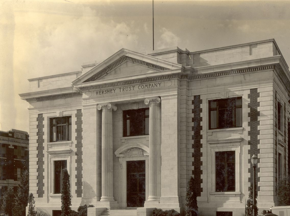 A sepia-toned vintage photograph of a neoclassical-style building featuring a triangular pediment and two grand pillars.