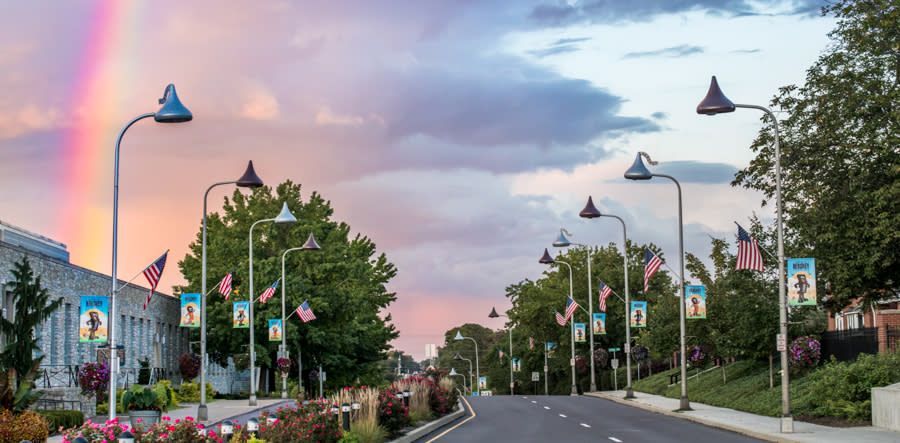 A street lined with Hershey's Kiss-shaped streetlights and American flags under a colorful rainbow sunset.