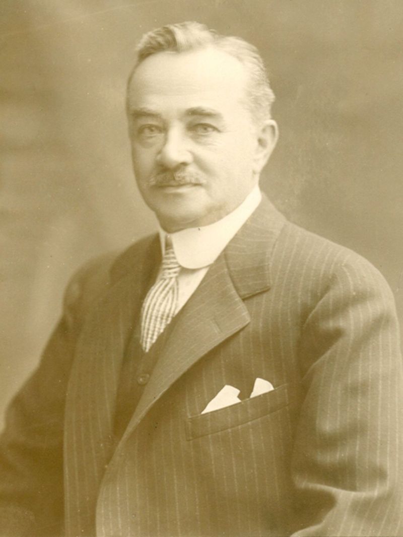 A sepia-toned portrait of a person in a pinstriped suit, vest, and tie with a pocket square.