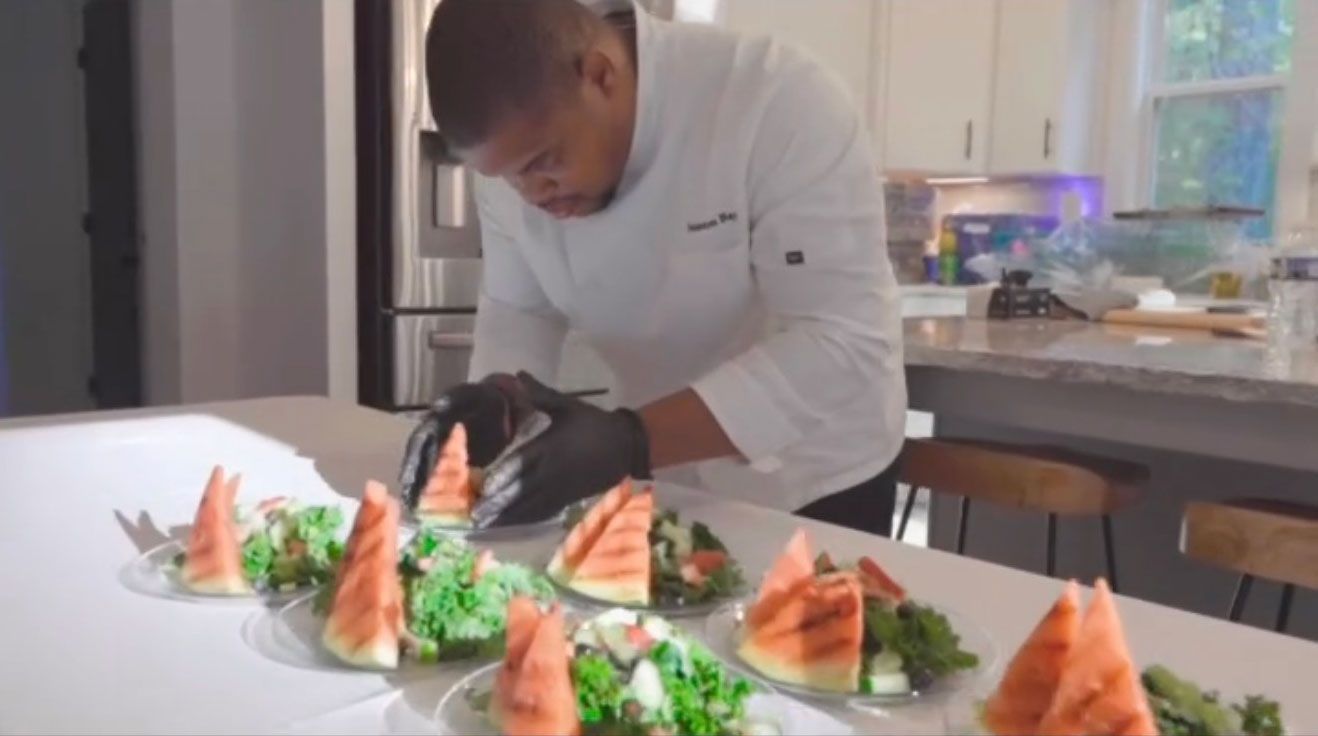 Chef plating salads with watermelon on a bright countertop, kitchen setting.