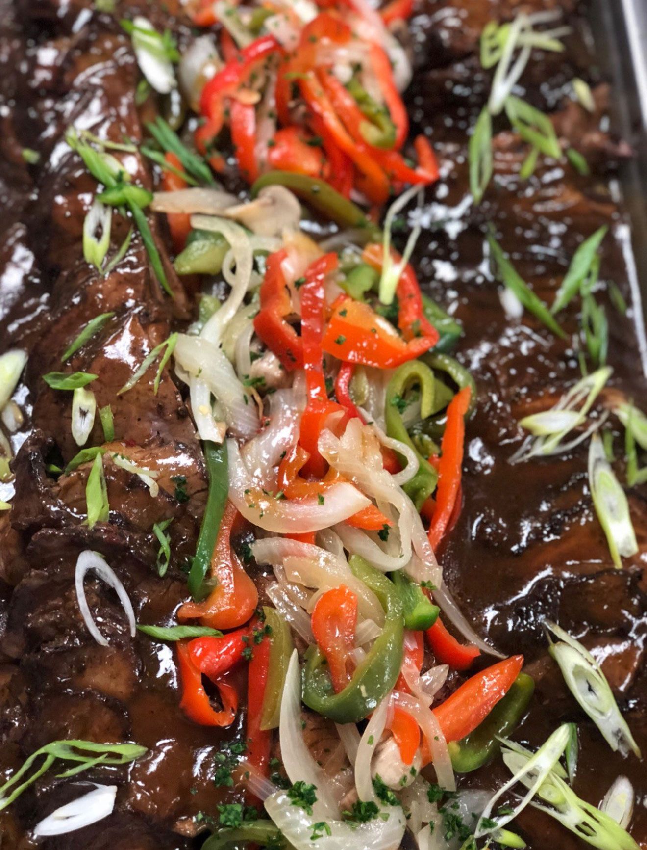 Beef with a rich sauce, topped with sautéed peppers, onions, and green onions.