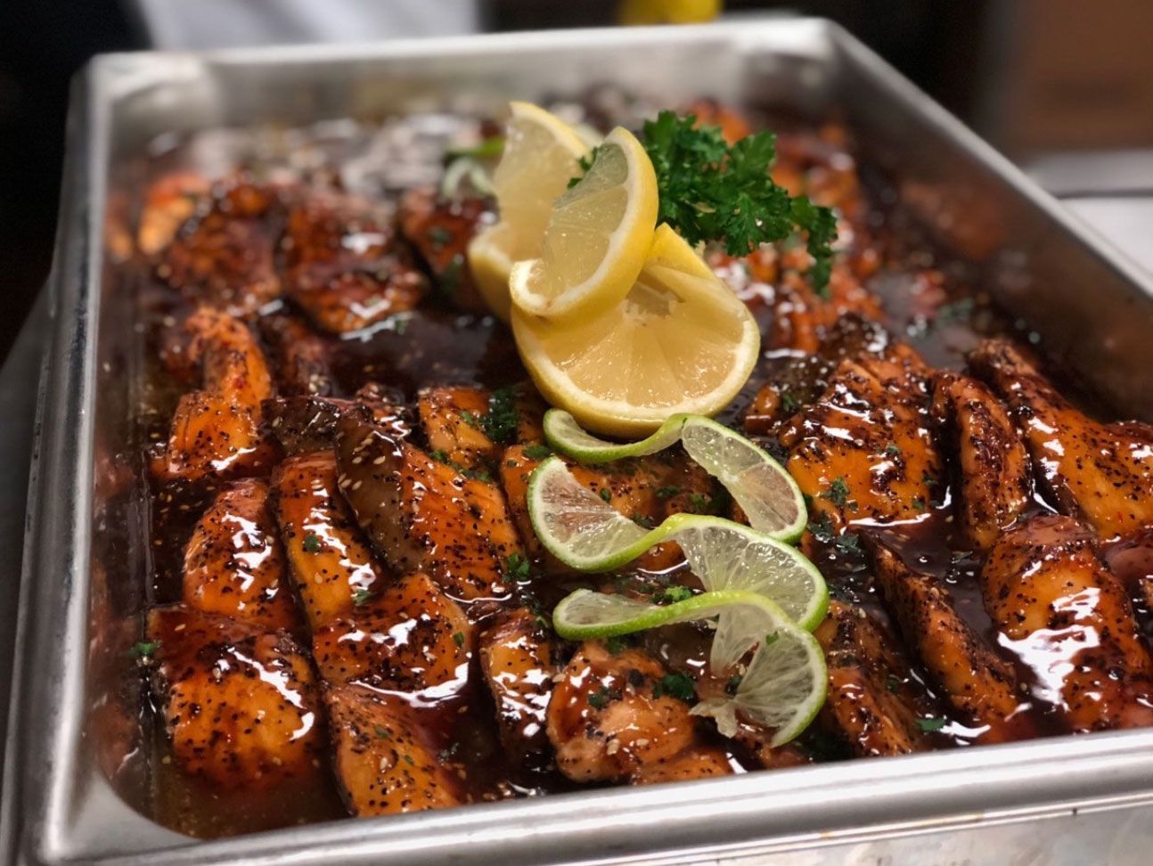 Pan of glazed salmon garnished with lemon and lime slices, and parsley.