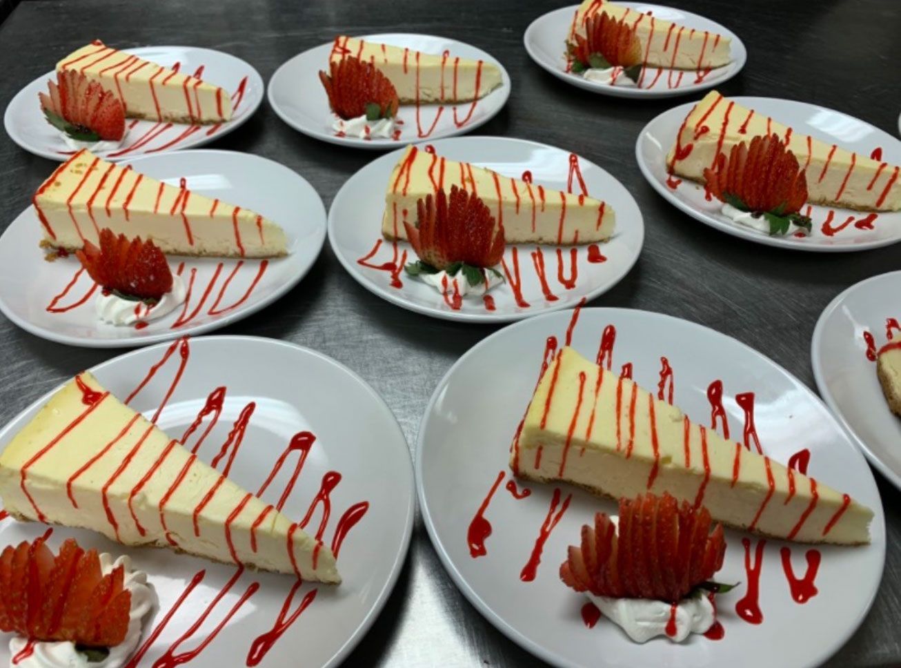 Plated cheesecake slices with strawberry garnish and red drizzle, ready for serving.