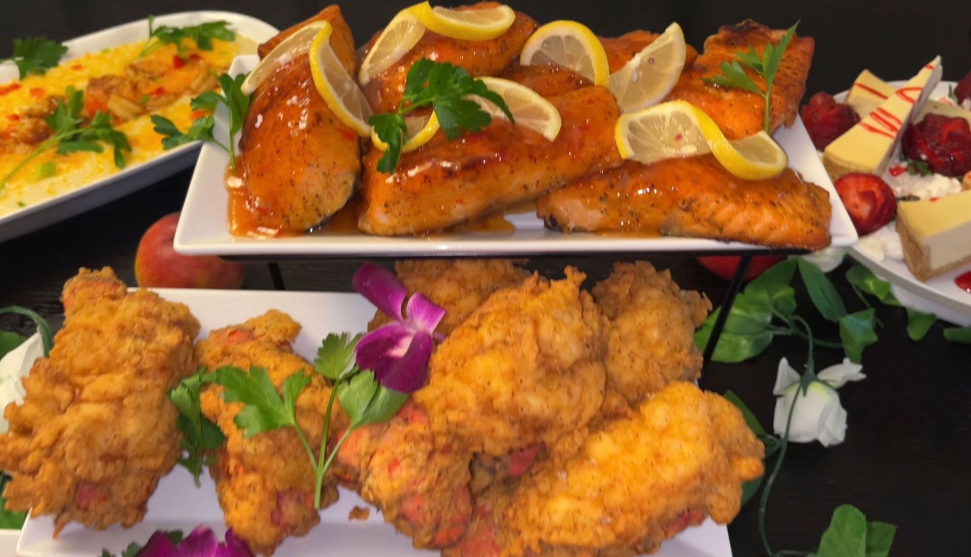 Platters of fried chicken, glazed salmon with lemon, a dessert plate of cheese and fruit, and a mango dish.