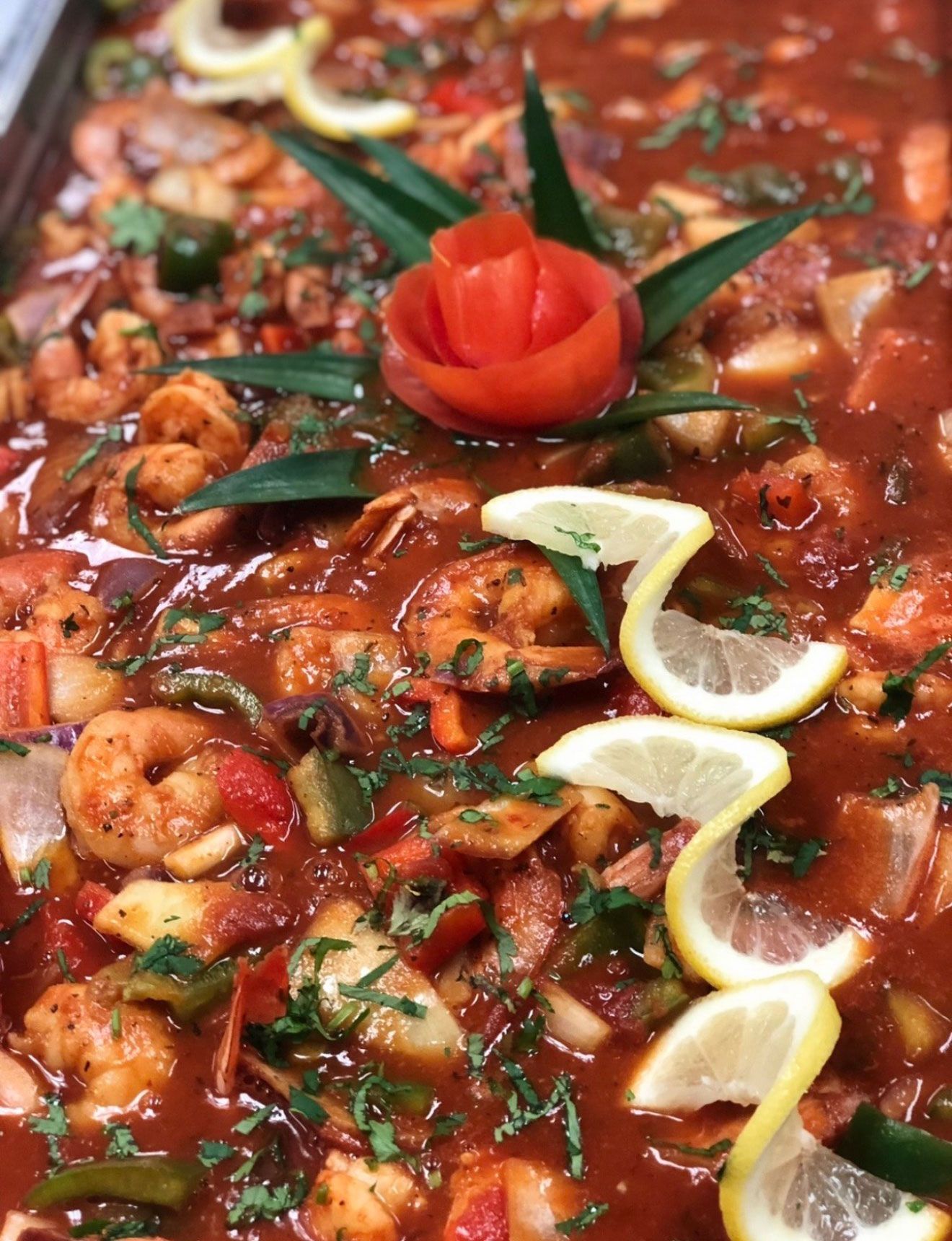 Shrimp in a red sauce with vegetables, garnished with lemon slices and a tomato flower.