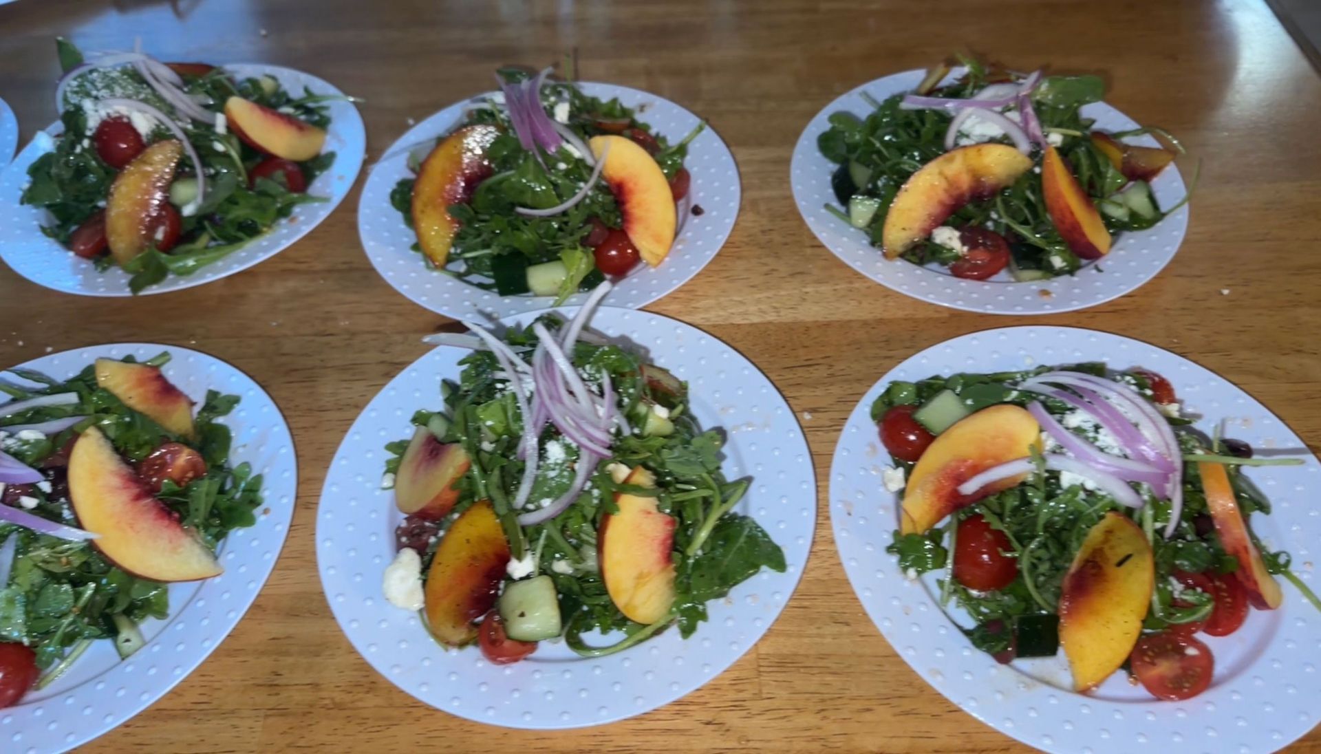 Six plates of salad with peaches, red onion, and tomatoes on a wooden table.
