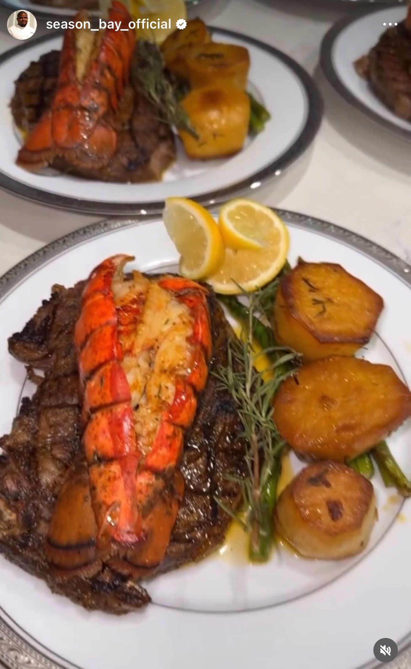 Surf and turf: steak with lobster tail, potato rounds, asparagus, lemon slices on a plate.