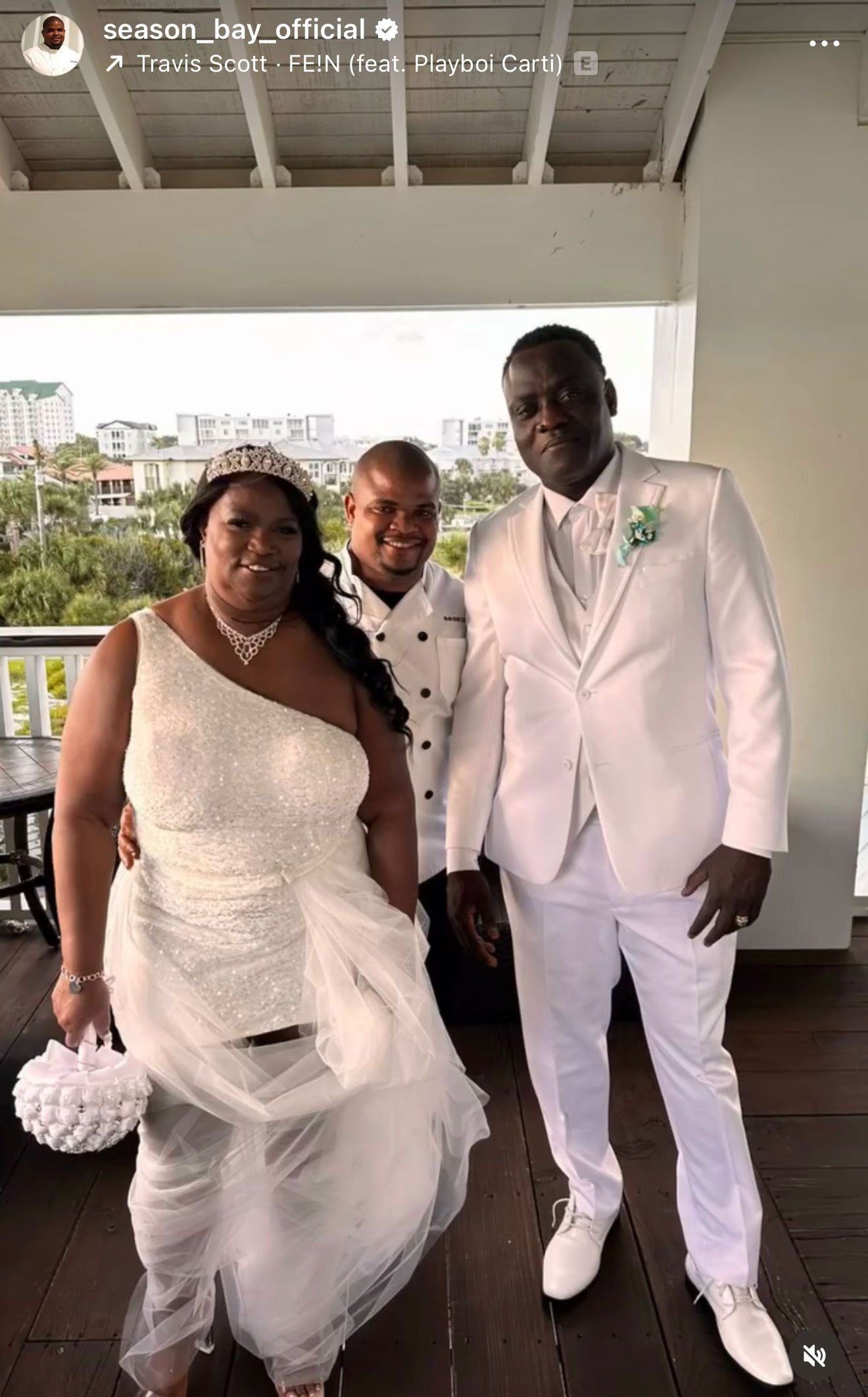 A newly married couple and officiant pose in wedding attire on a patio.