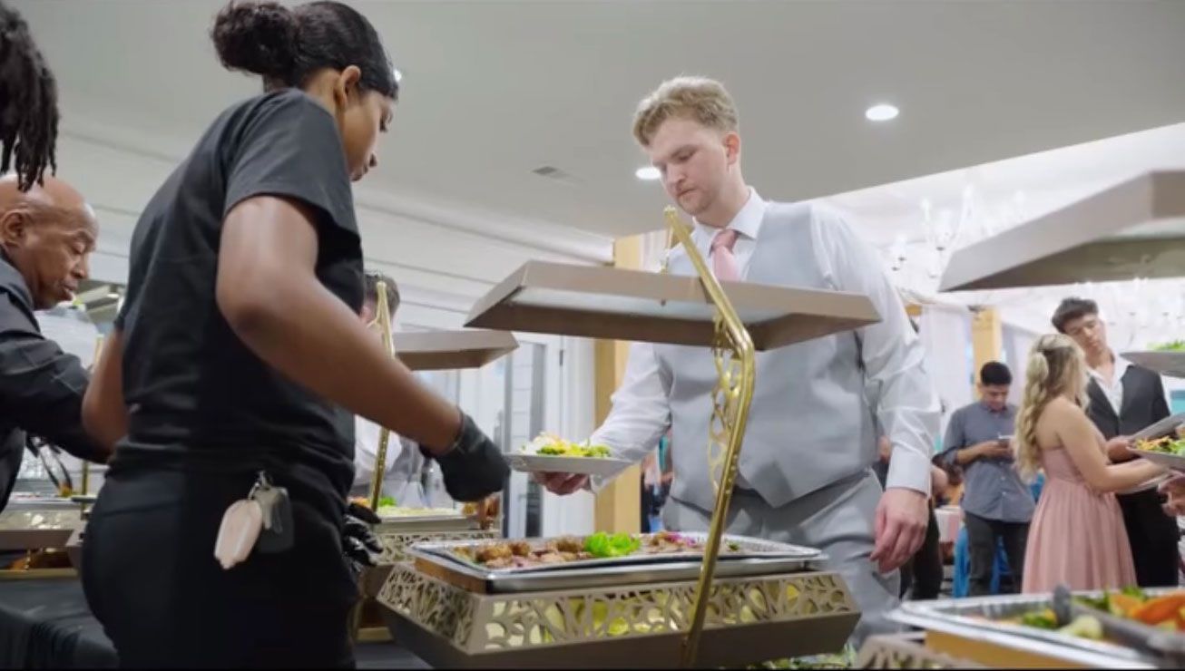 A wedding buffet with servers in black and guests selecting food.