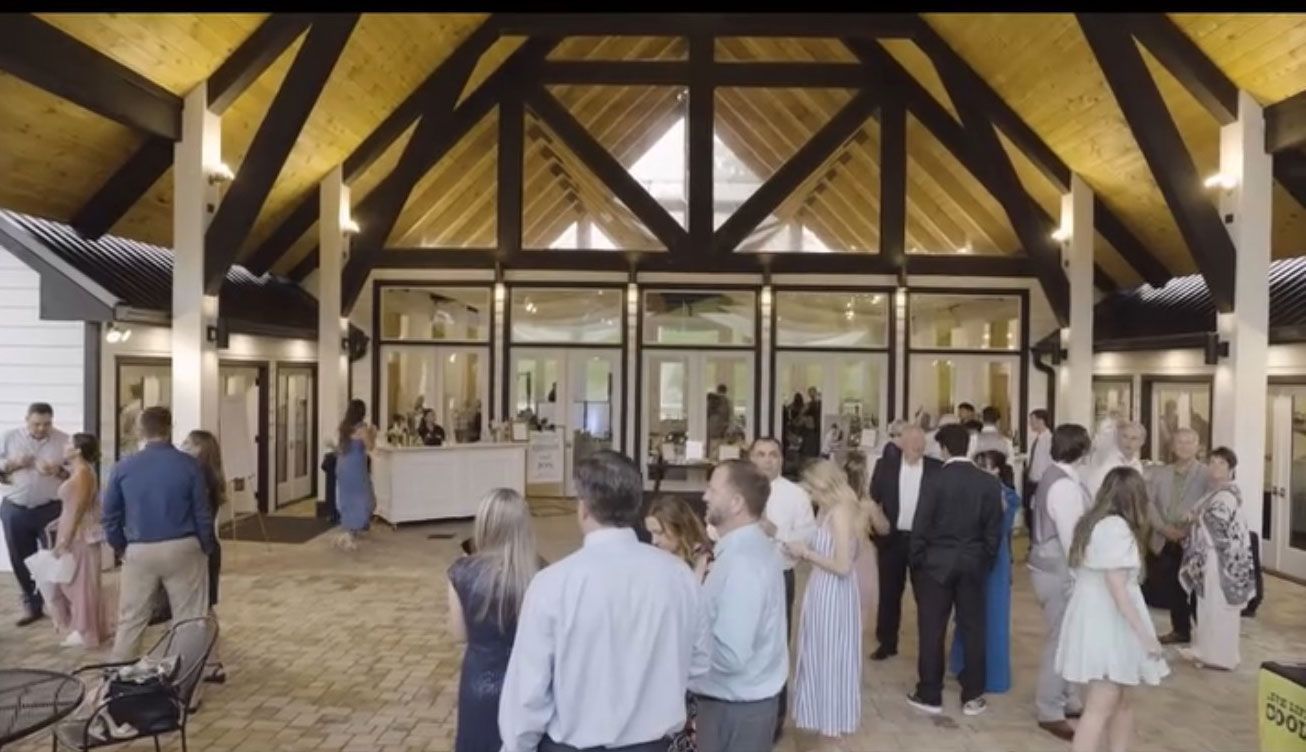 Guests at a wedding reception, open-air venue with a high ceiling and windows.