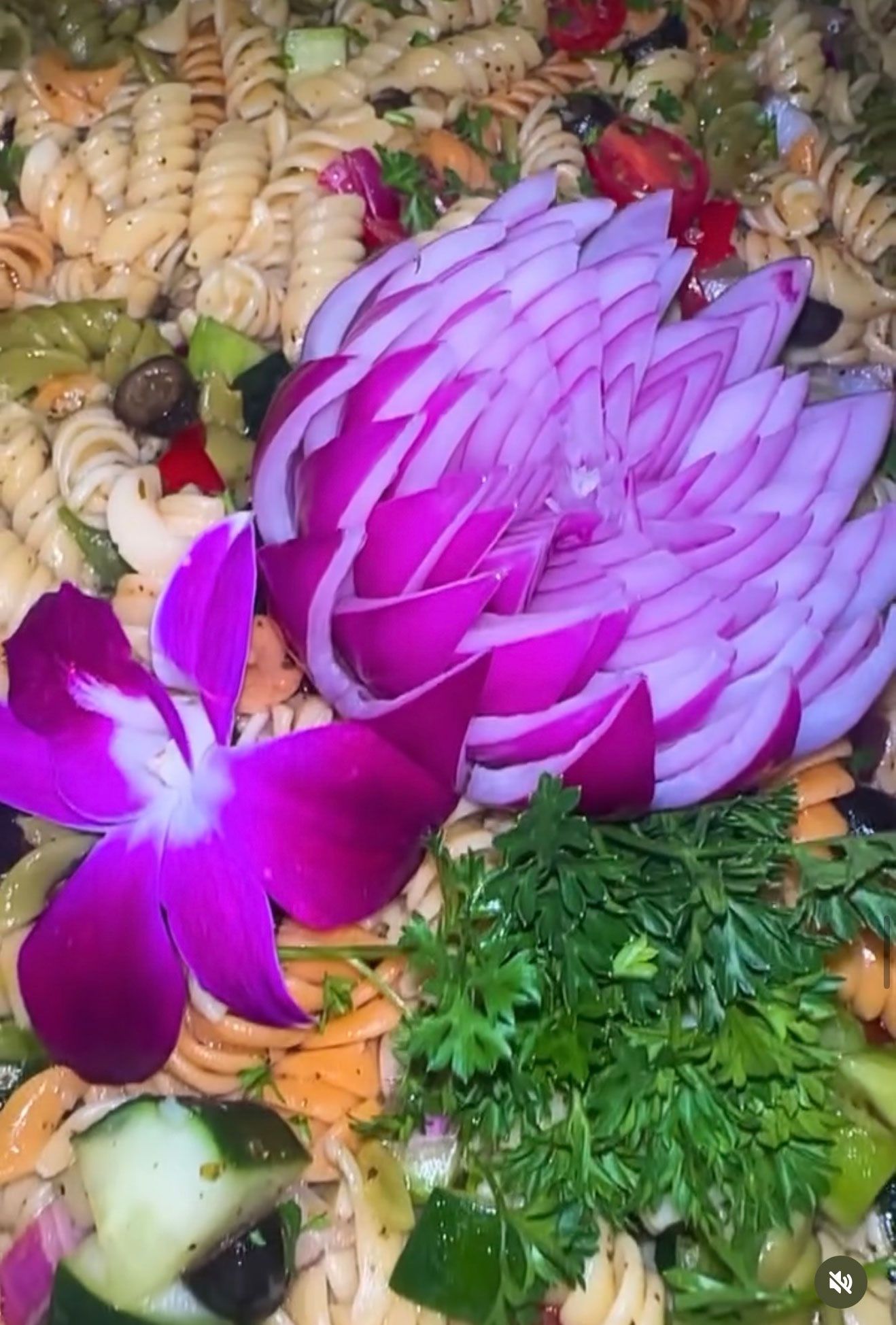 Pasta salad with a carved red onion garnish and a purple orchid.