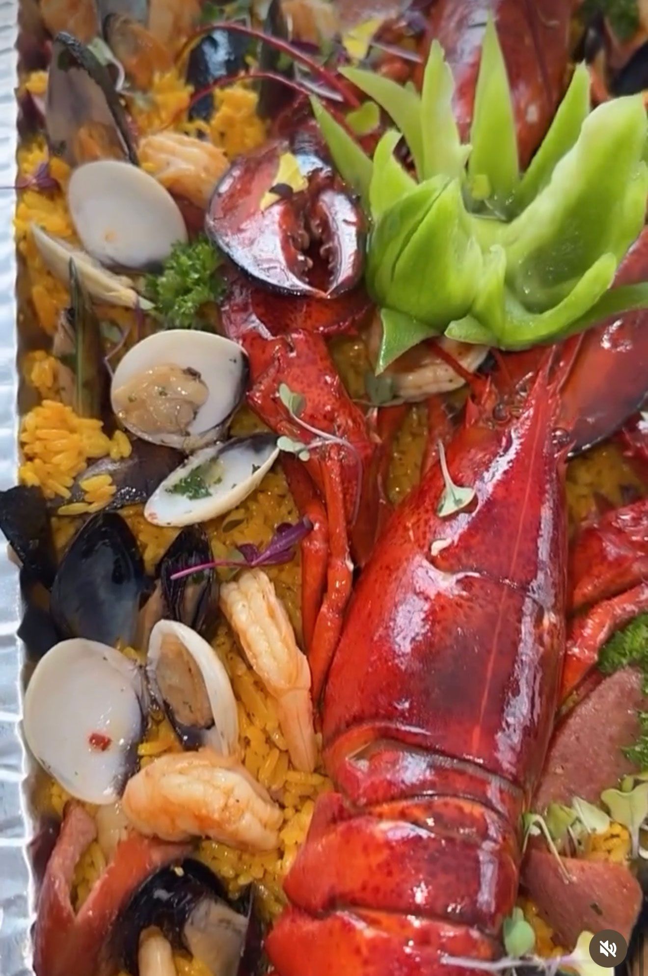 Paella with lobster, clams, mussels, shrimp, and a carved green pepper garnish.