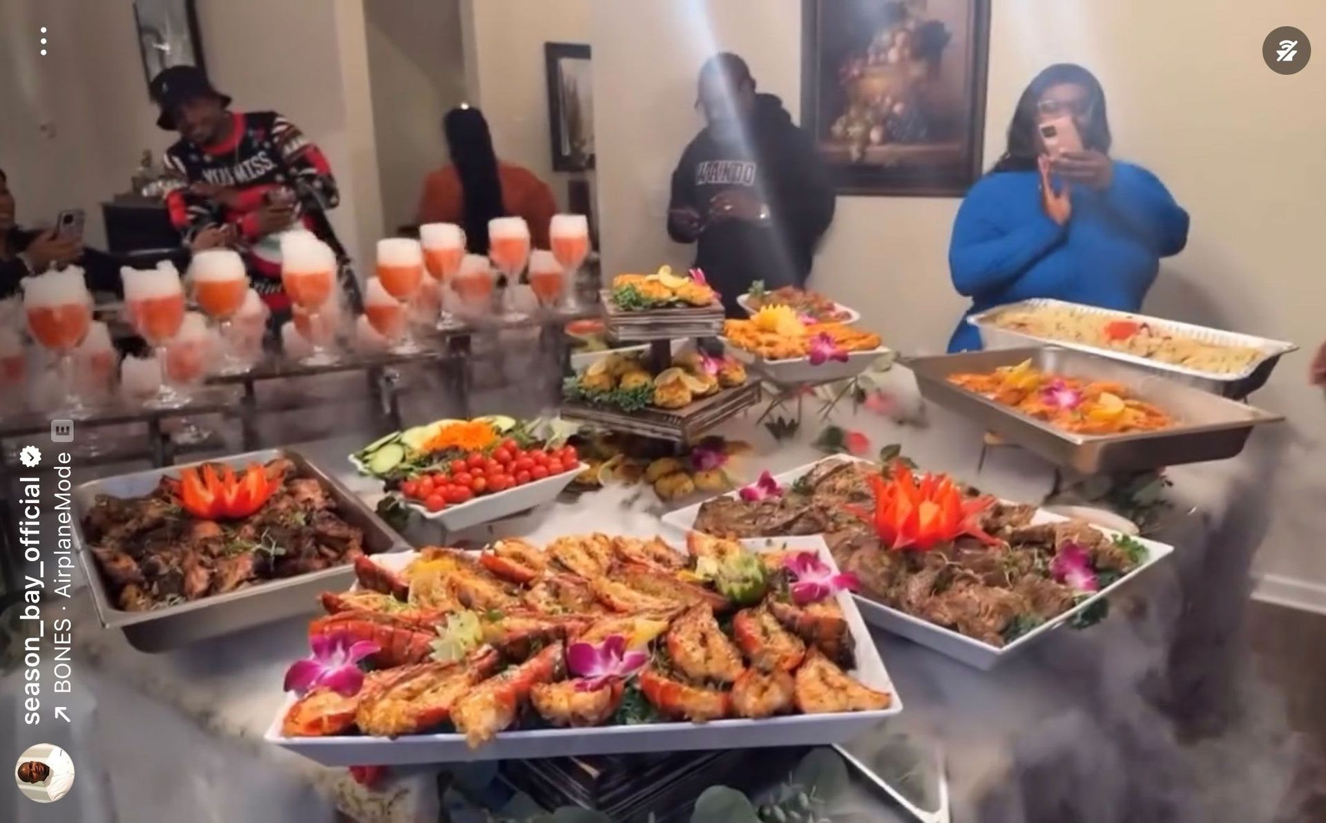 Buffet with various food dishes, people serving themselves, in a crowded space.
