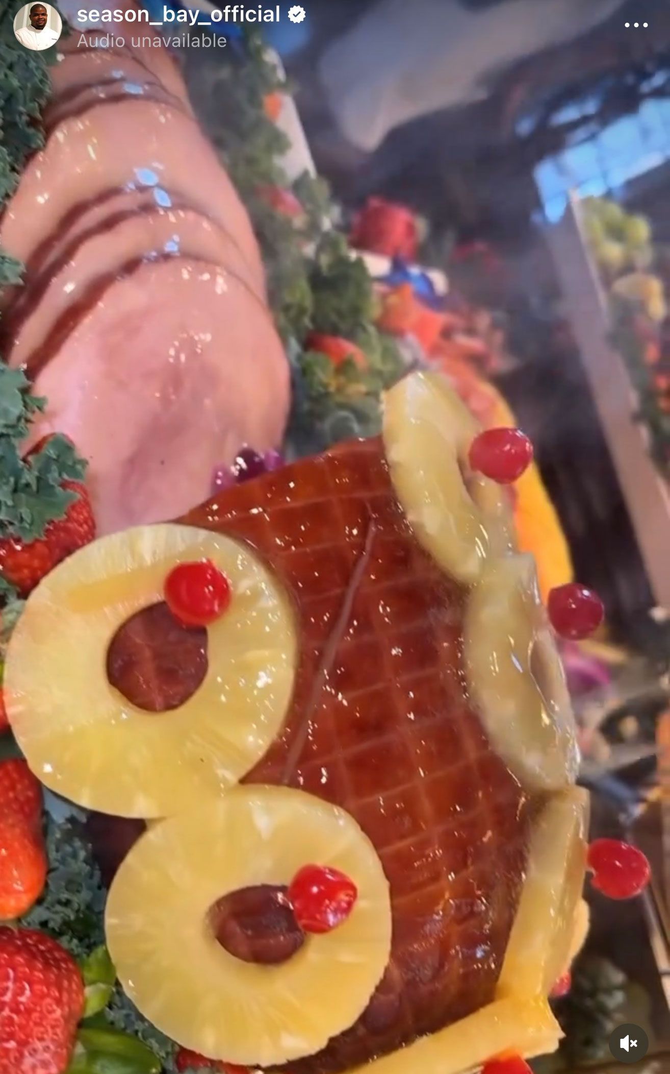 Glazed ham decorated with pineapple rings and cherries, displayed with fruit and greens.