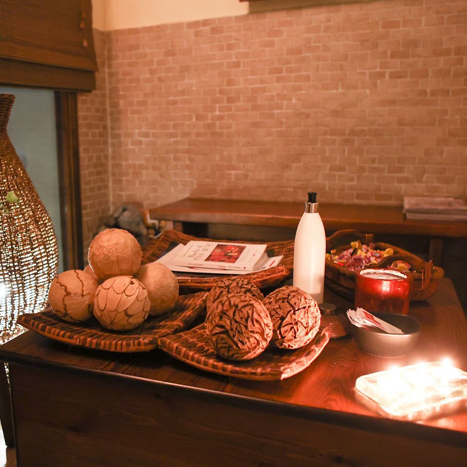 L'interno di una spa, illuminato da luci soffuse, è arredato con sfere decorative di paglia in cestini intrecciati, una bottiglia di lozione bianca e candele accese.