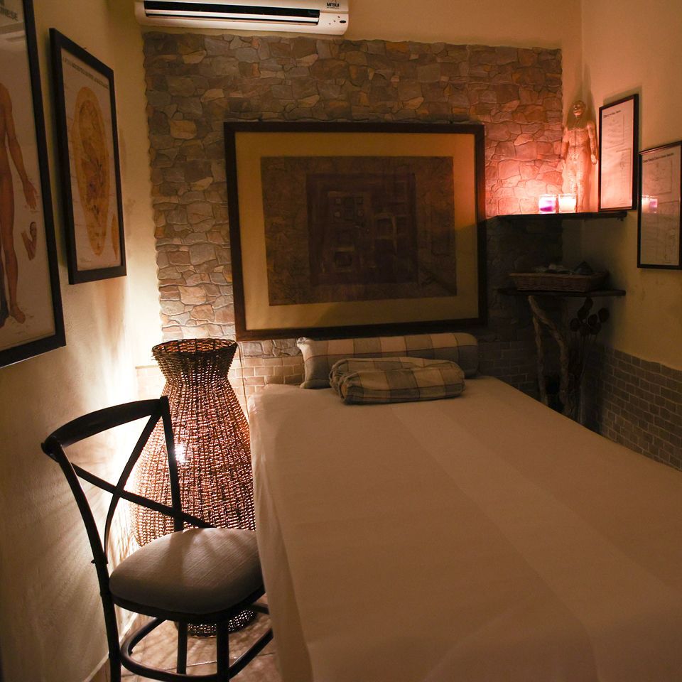 Una sala massaggi con luci soffuse, lettino per trattamenti, sedia in legno, pareti in pietra e una calda illuminazione ambientale.