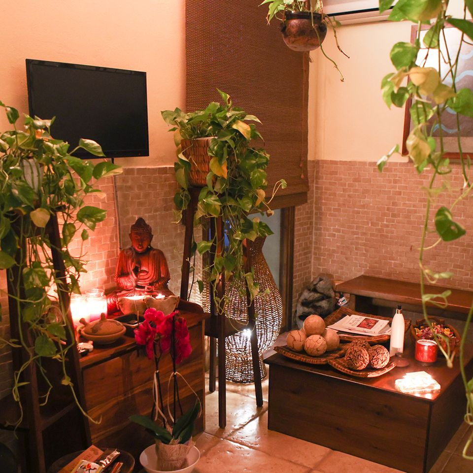 Sala benessere illuminata da una luce calda, con piante sospese, una piccola statua di Buddha, mobili in legno e sfere decorative in pietra.