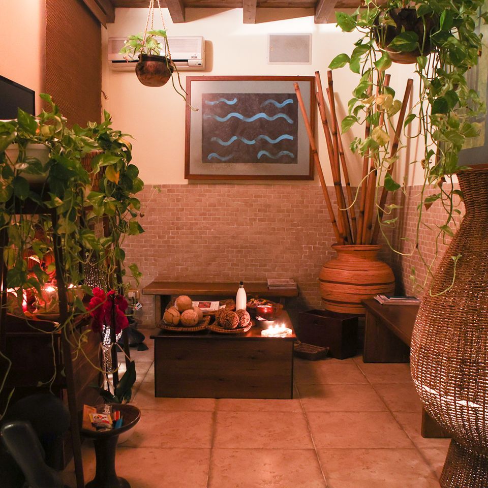 Un'accogliente sala d'attesa della spa, illuminata da luci soffuse, con rigogliose piante in vaso, un tavolino in legno con candele e decorazioni intrecciate.