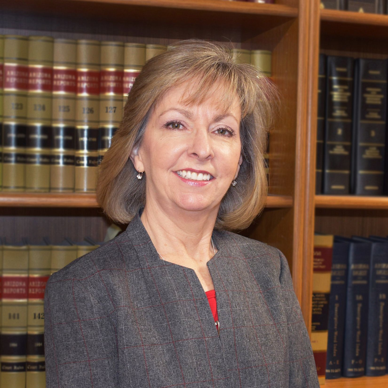 Woman in a blazer smiles, standing in front of a bookcase filled with law books.