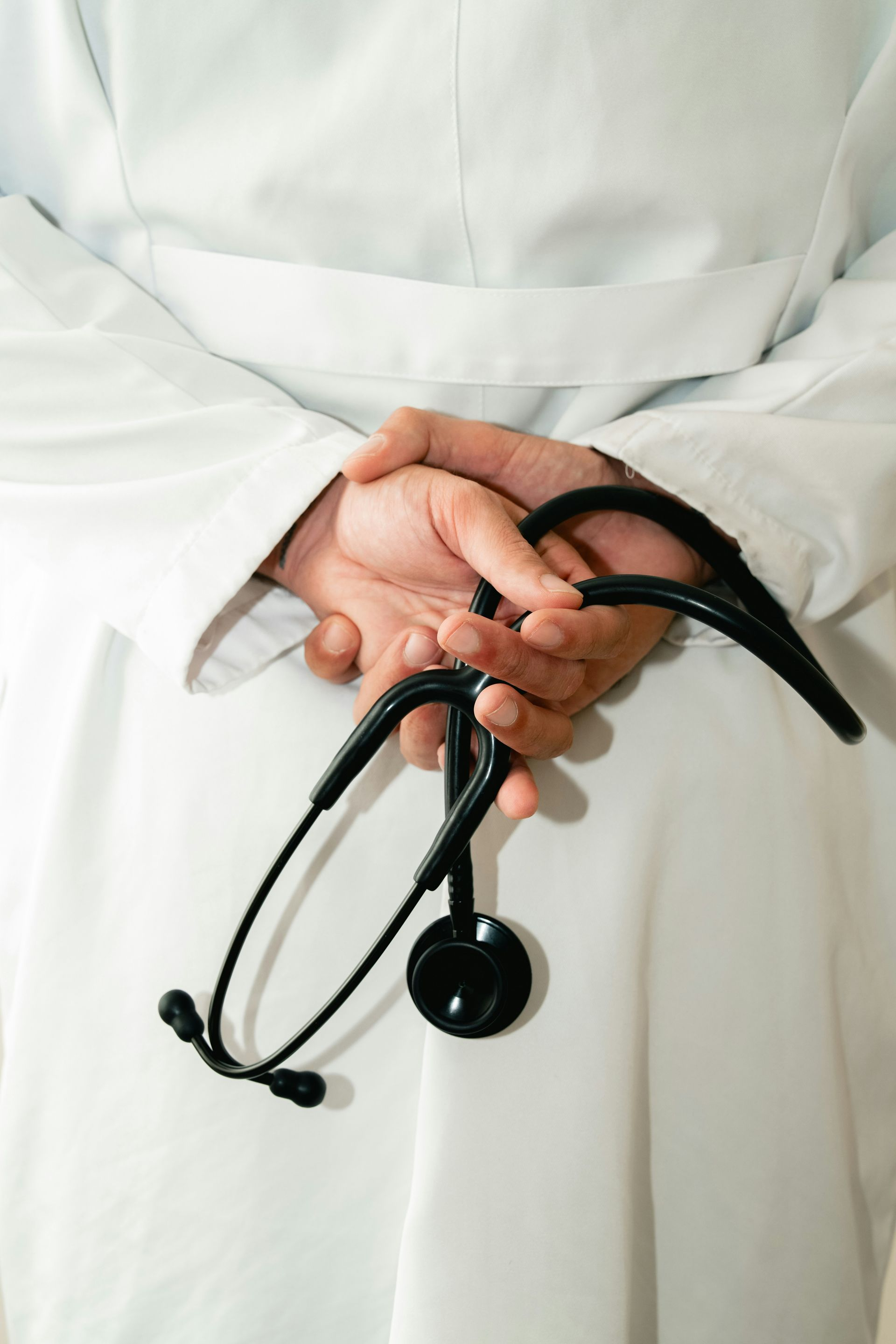 Person in white coat, hands behind back holding stethoscope.