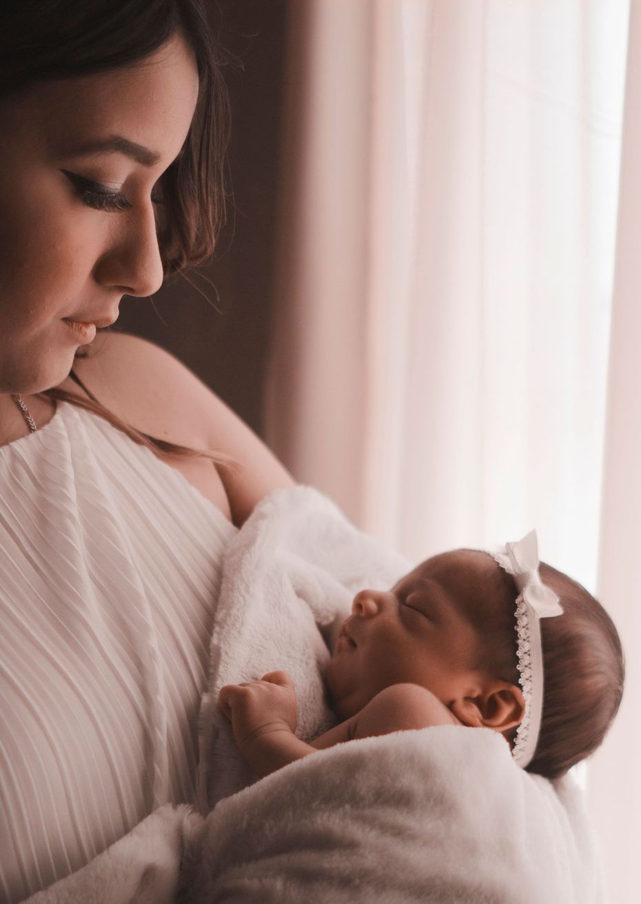 Woman gently holding a swaddled newborn near a bright window