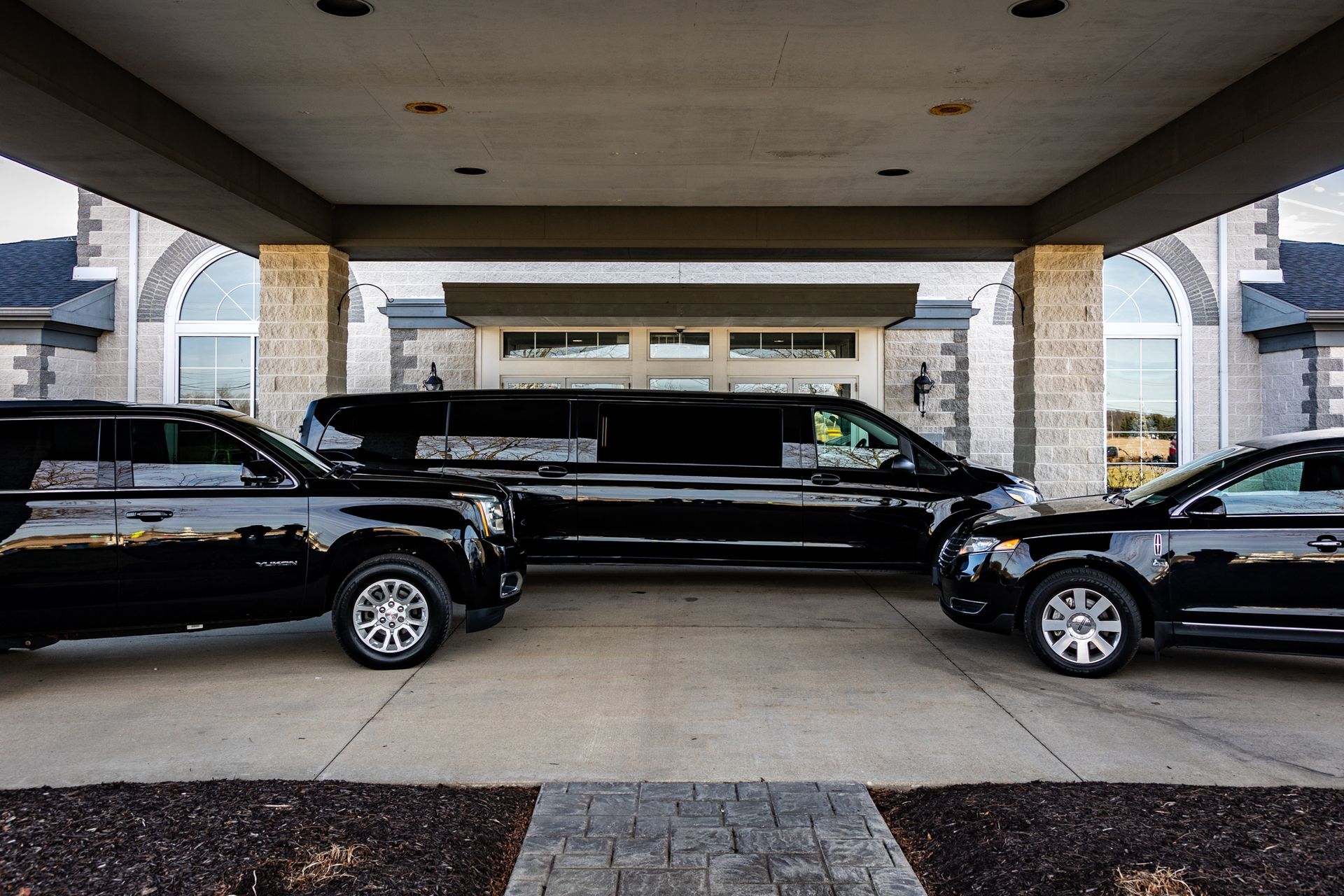 Two black limousines are parked under a canopy in front of a building.