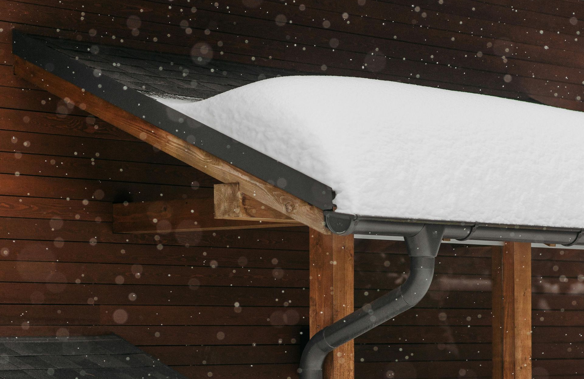 Snow-covered roof overhang with a gutter, and snow falling against a wood-paneled wall.