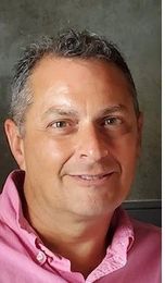 Man with short graying hair, smiling, wearing a pink button-down shirt.