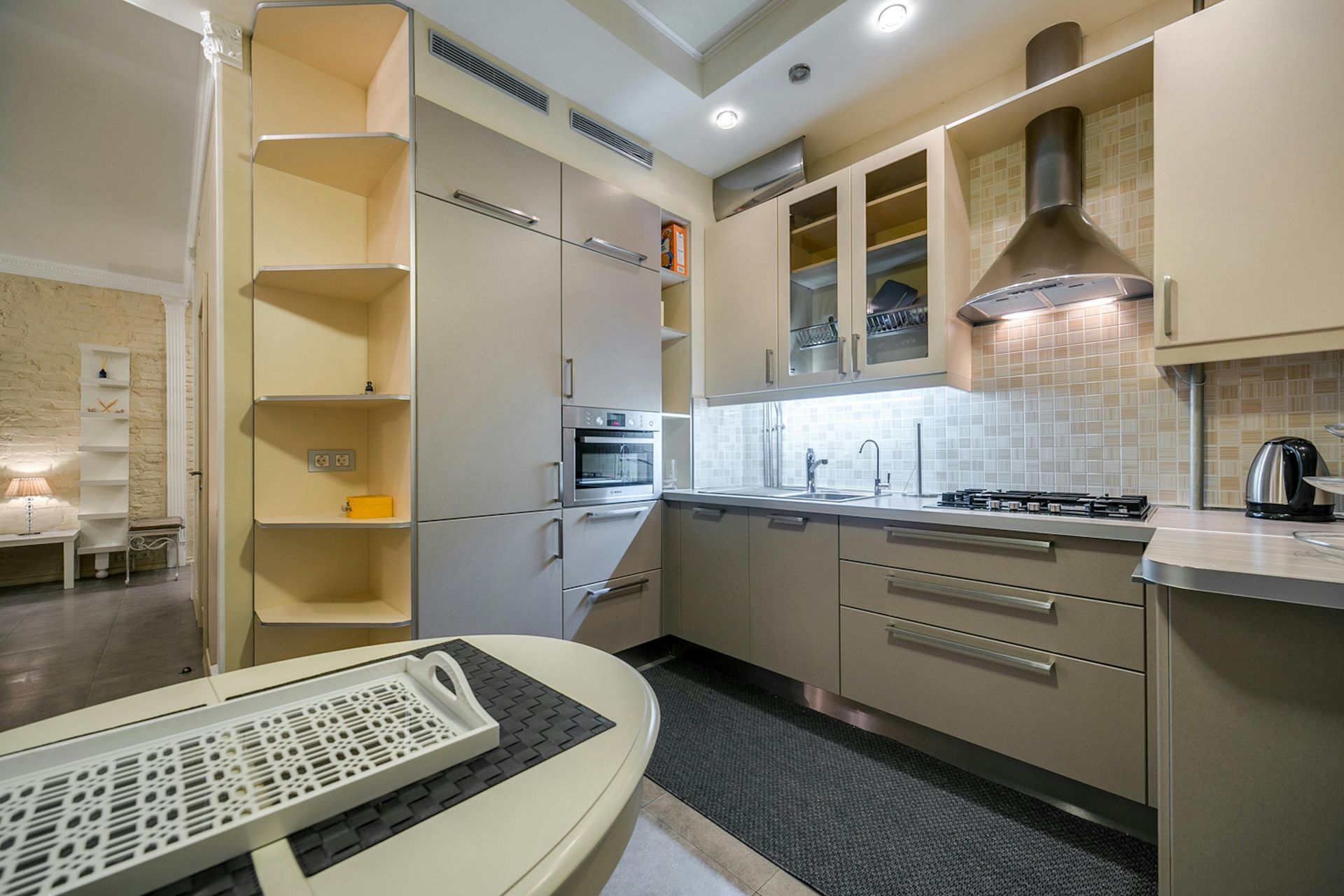 Modern kitchen with beige cabinets, stainless range hood, tiled backsplash, and built-in shelving