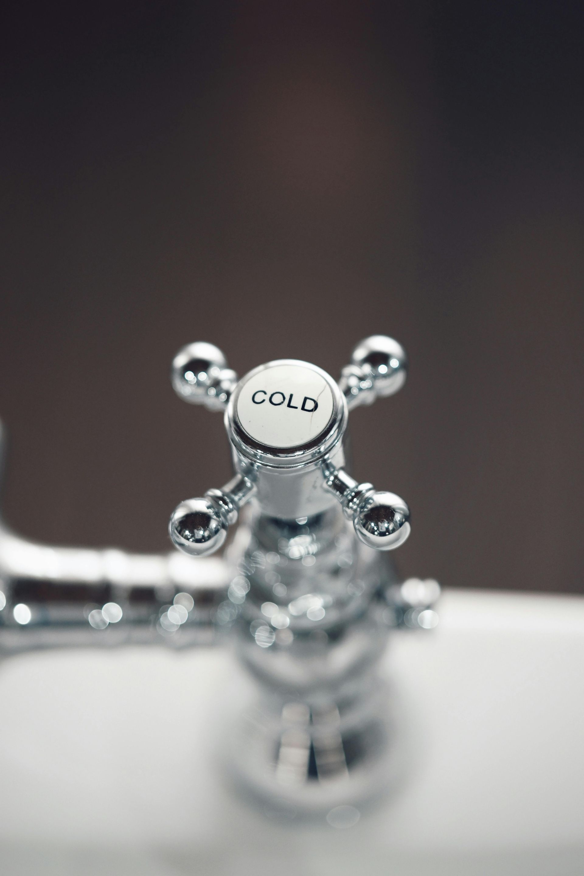 Chrome faucet handle labeled “COLD” on a sink faucet, close-up.