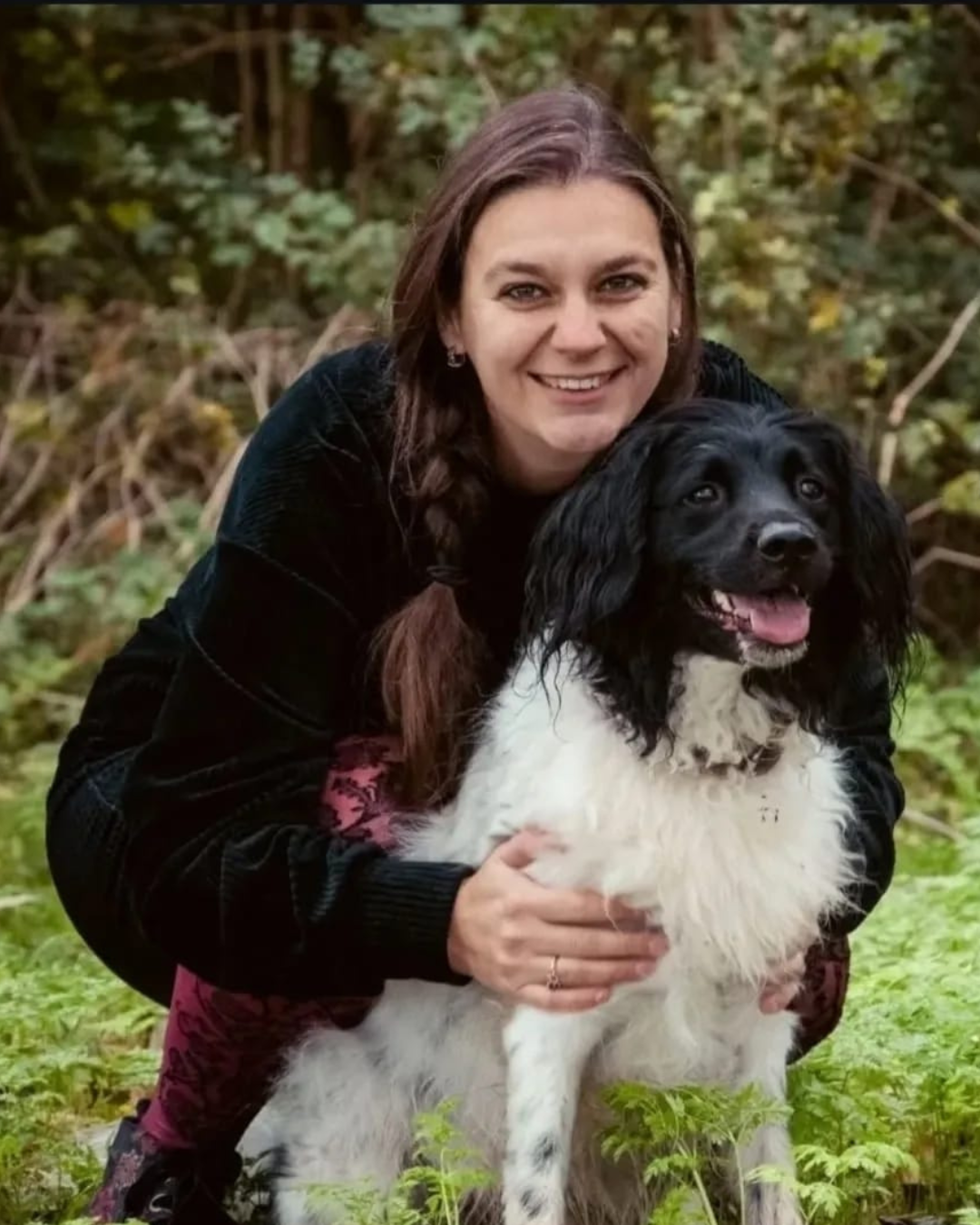 Een vrouw knuffelt een zwart-witte hond in het bos.