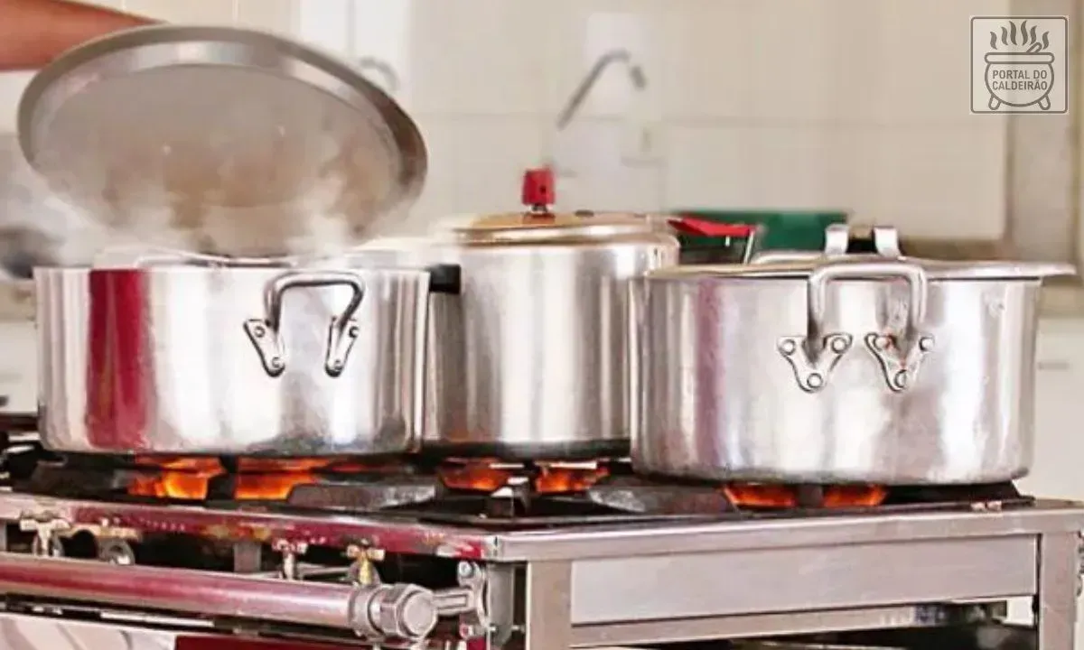 Imagem de Panelas comuns sobre um fogão comercial a gás com chamas amarelas.