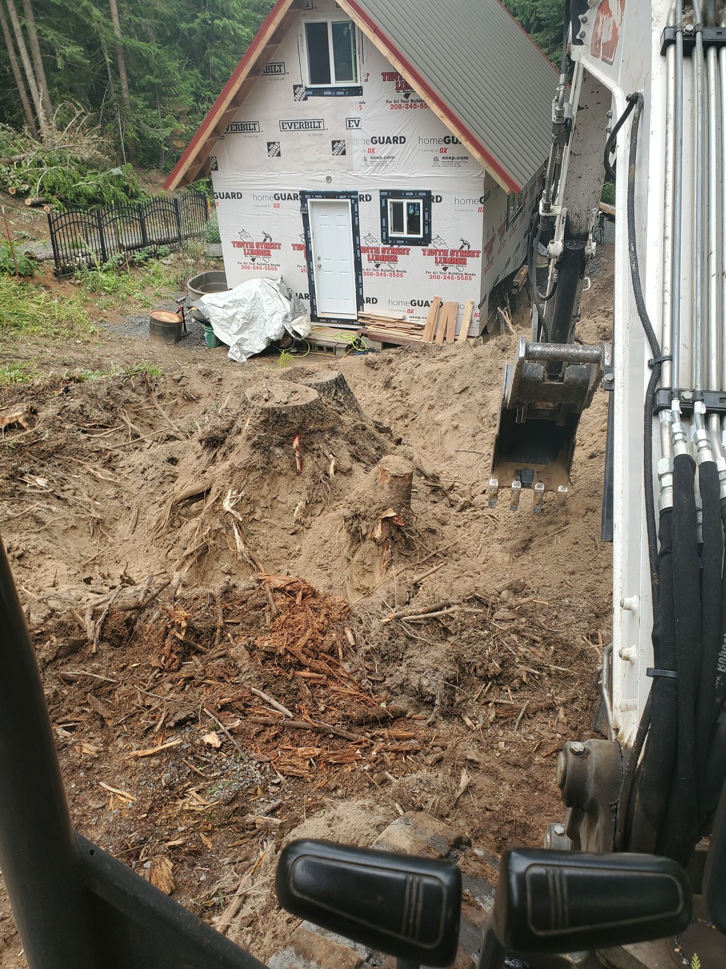 Excavator digging near a small unfinished house. Earth and debris surround the construction site.