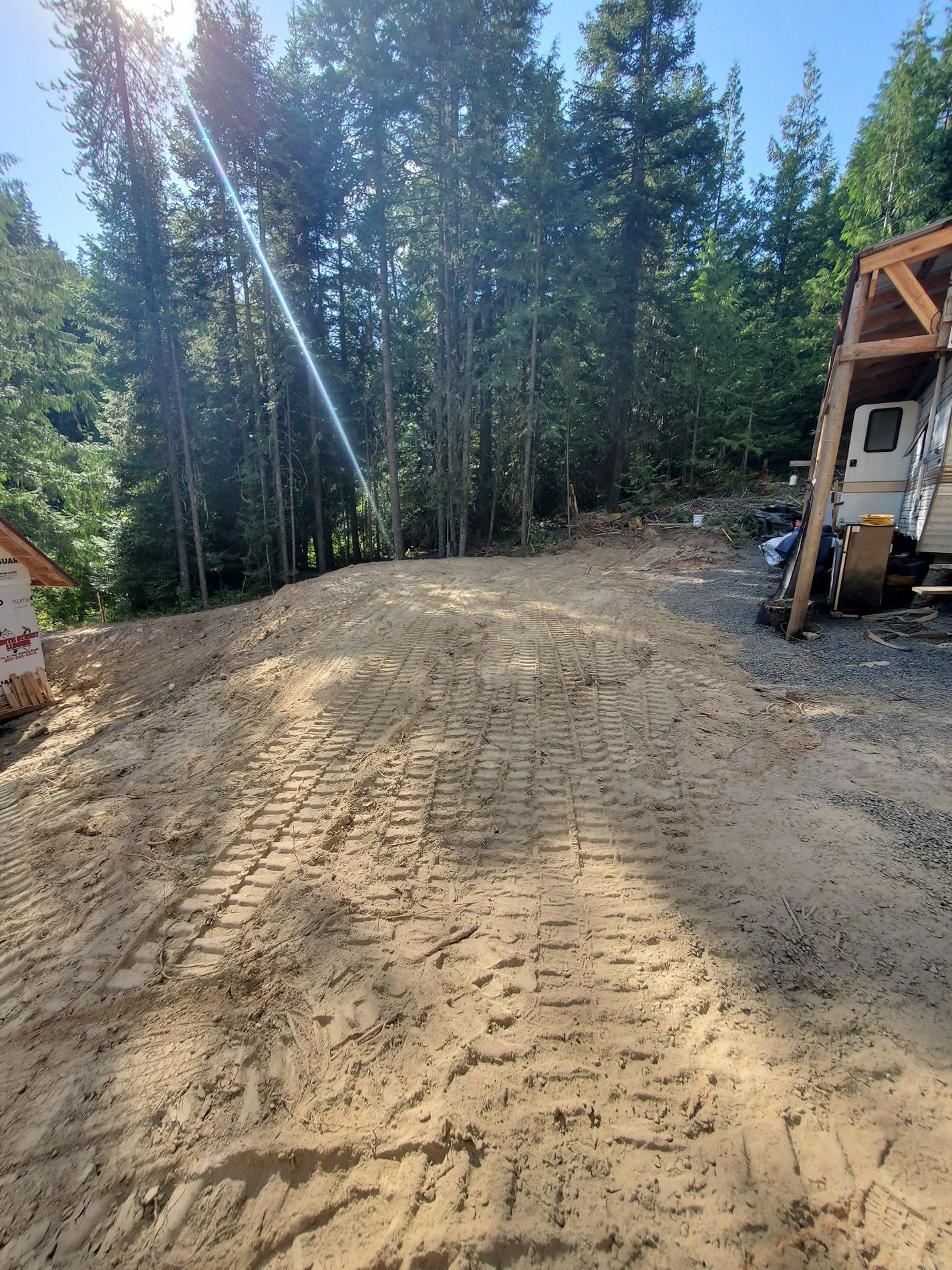 Dirt road in a forest clearing with construction materials and trees. Sunny day.