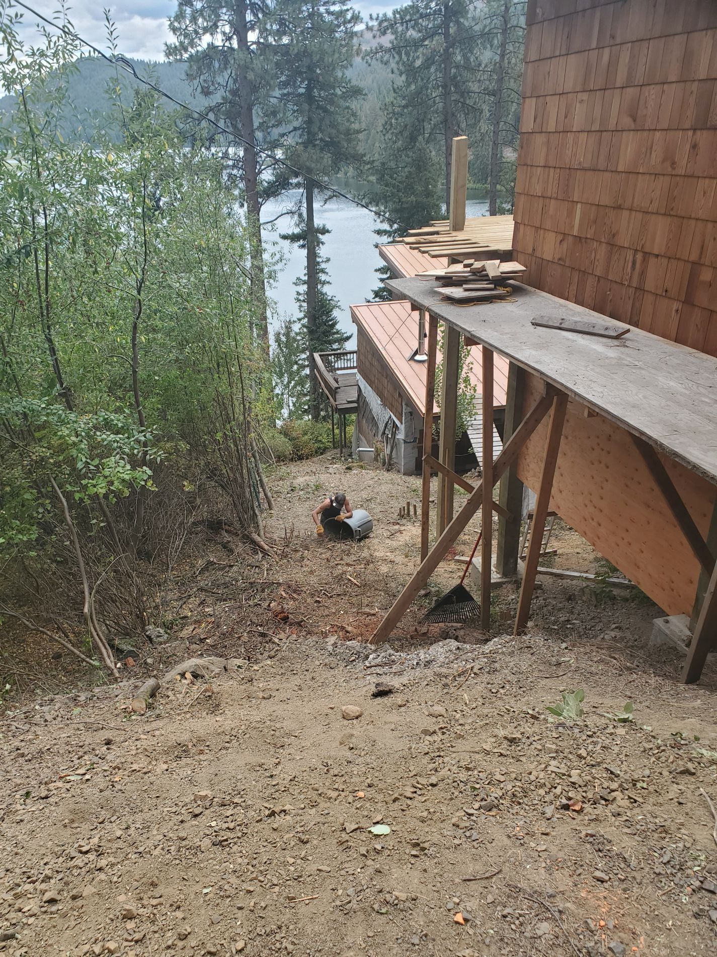 Dirt path slopes down to a lake, passing a wood-framed deck under construction.