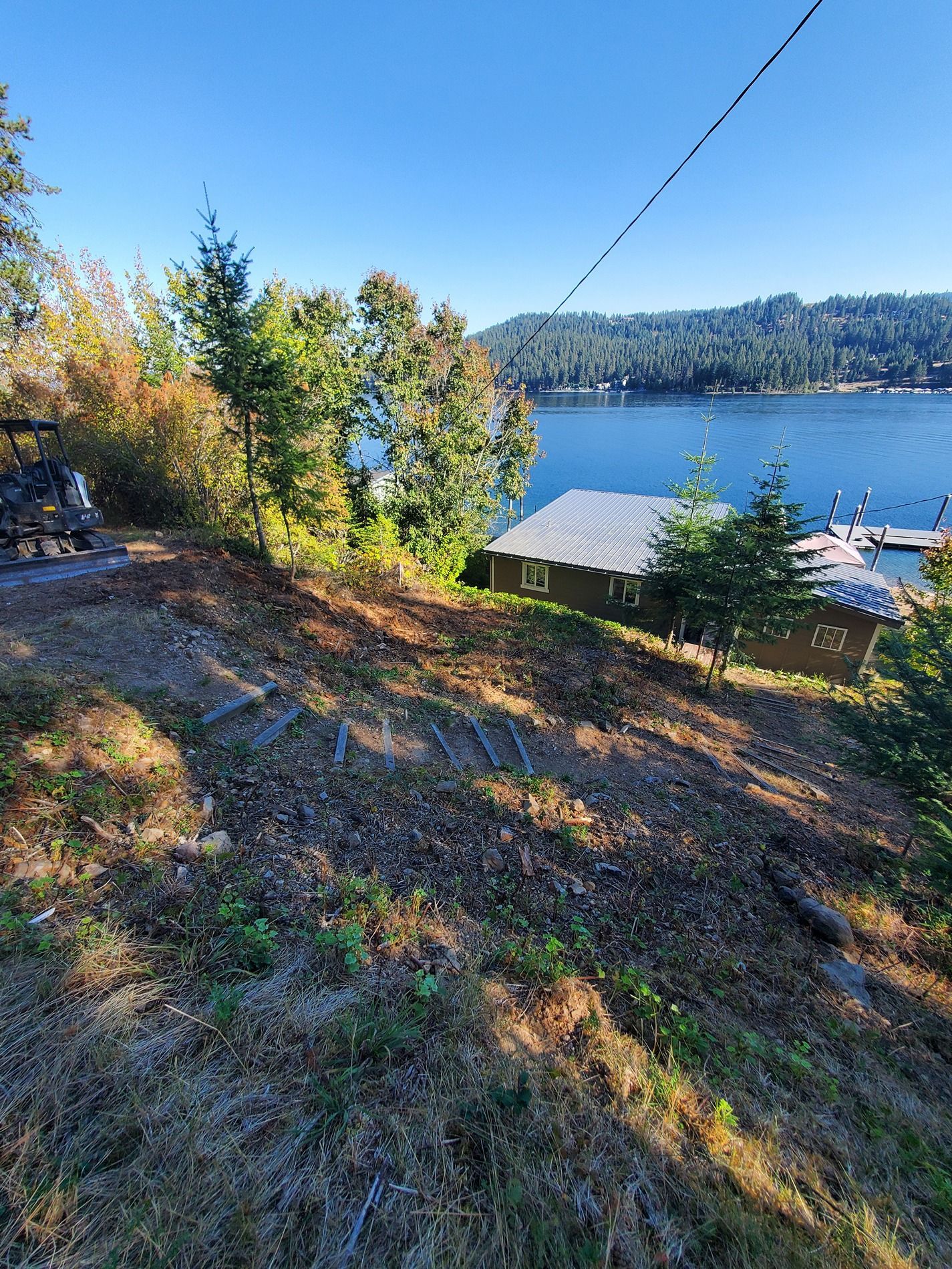 A hillside view of a lake and shoreline with trees and a building. Sunny day.