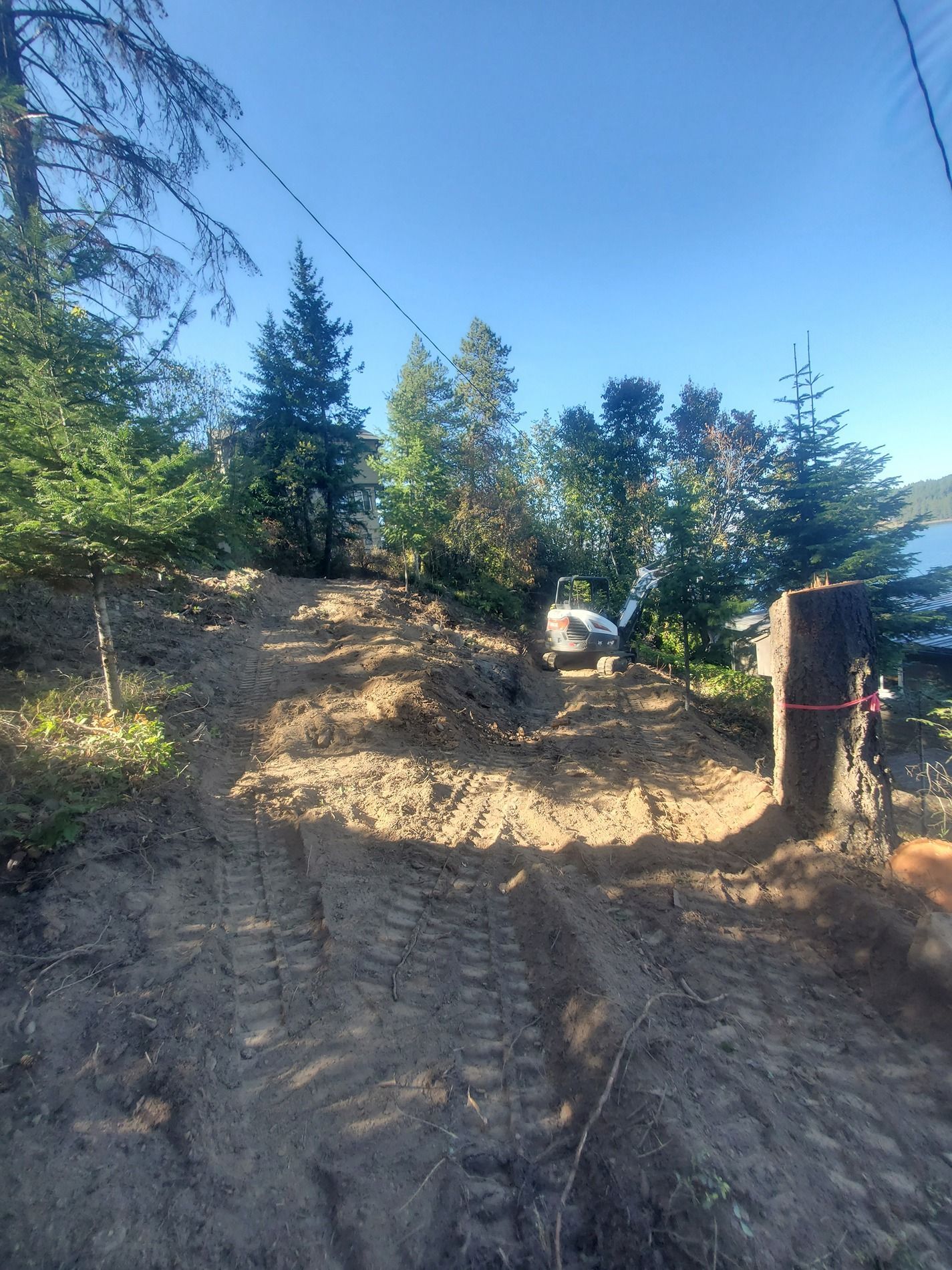 Dirt path leading to a vehicle parked near trees, with a lake visible in the background. Bright sunny day.