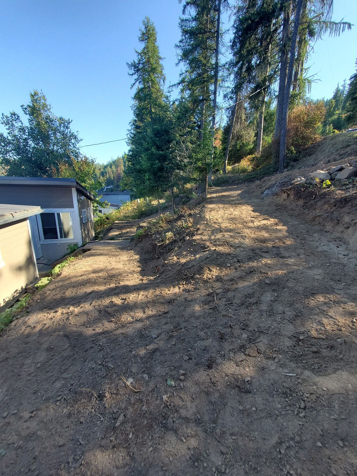 Dirt path leading downhill, next to a building. Trees and a lake are visible in the background.