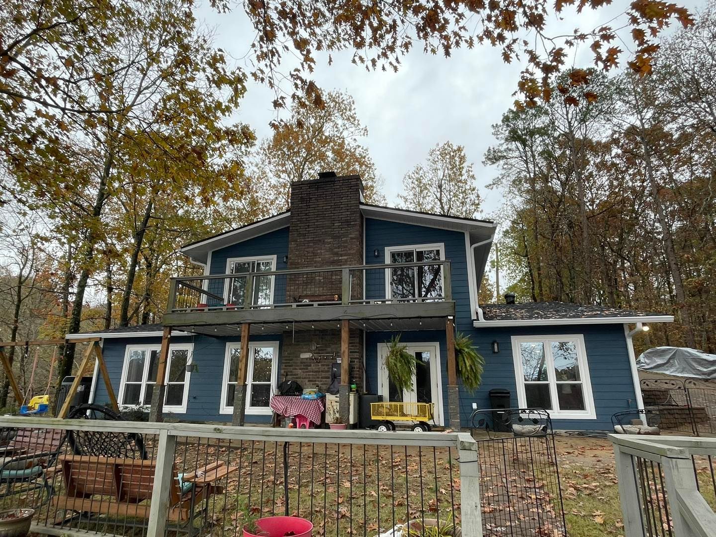 A large blue house is surrounded by trees and a fence.
