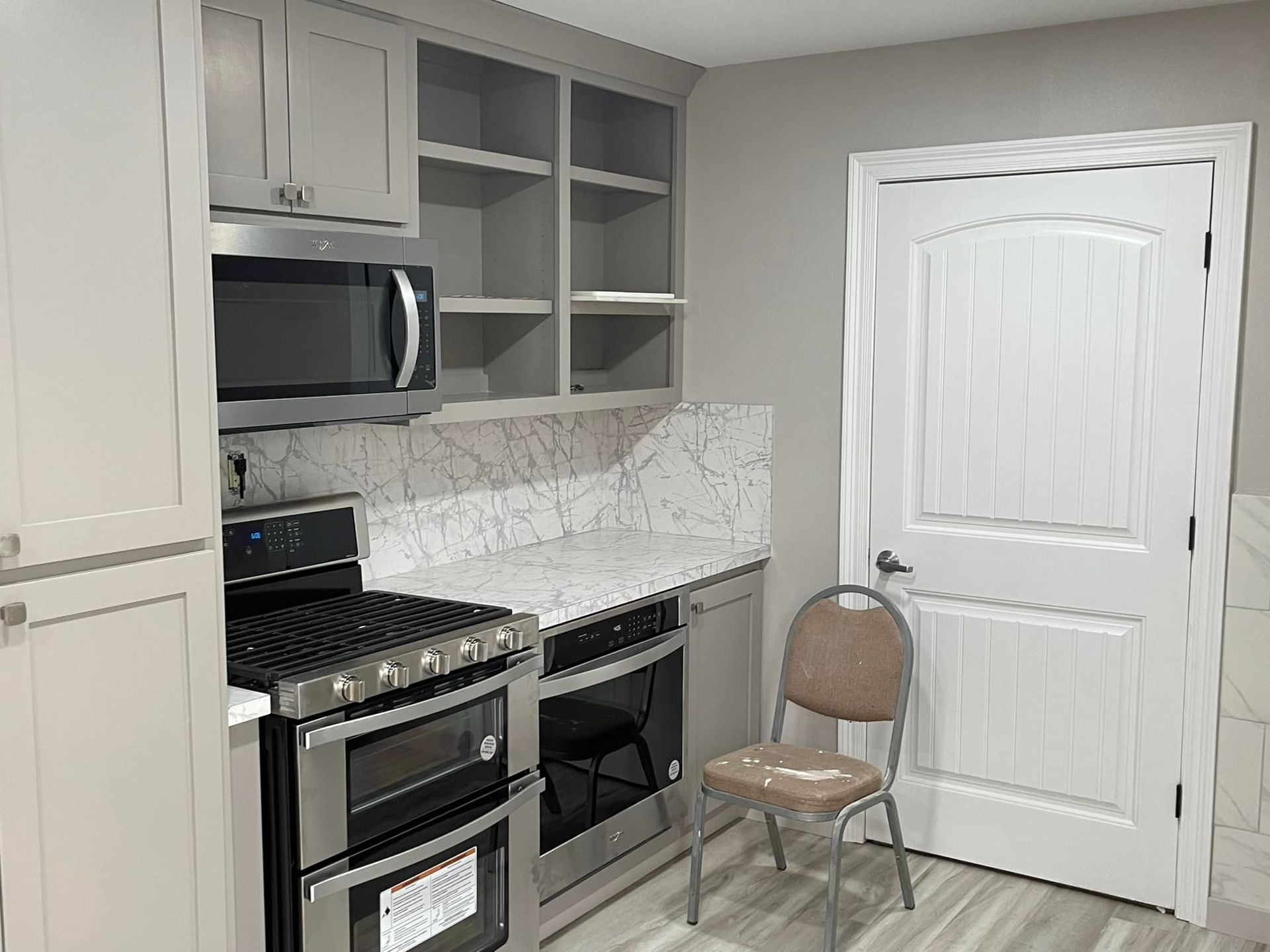 A kitchen with a stove , oven , microwave and chair.
