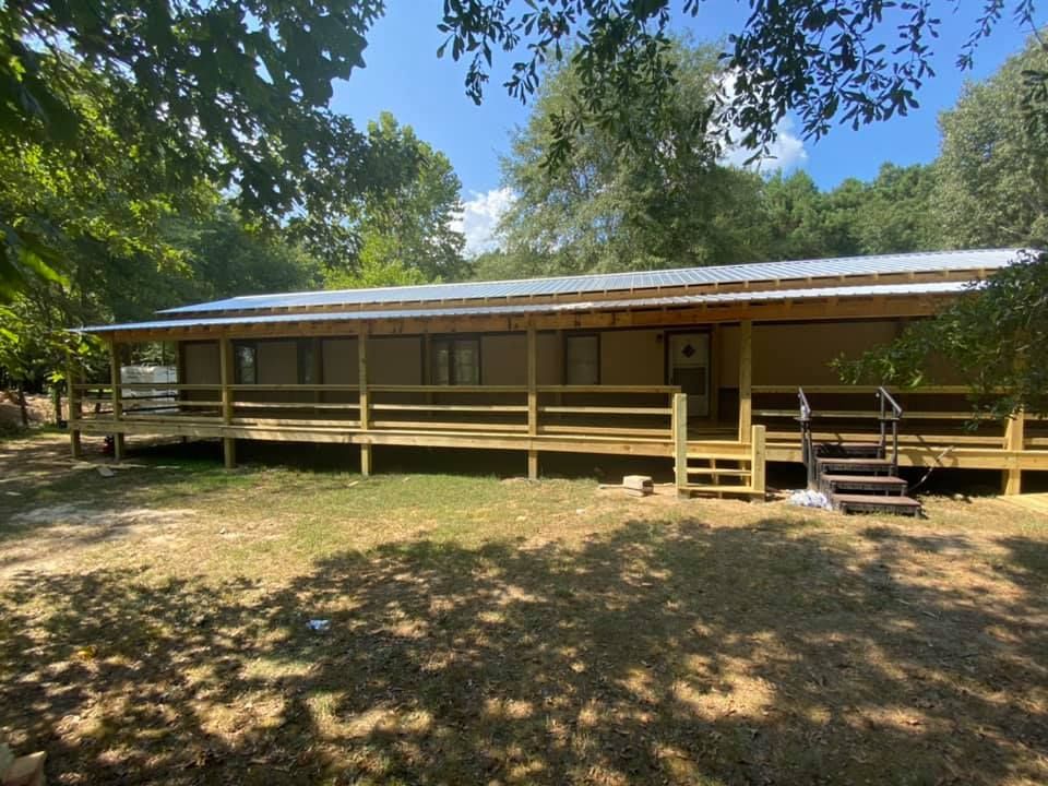 A house with a large porch and stairs is surrounded by trees.