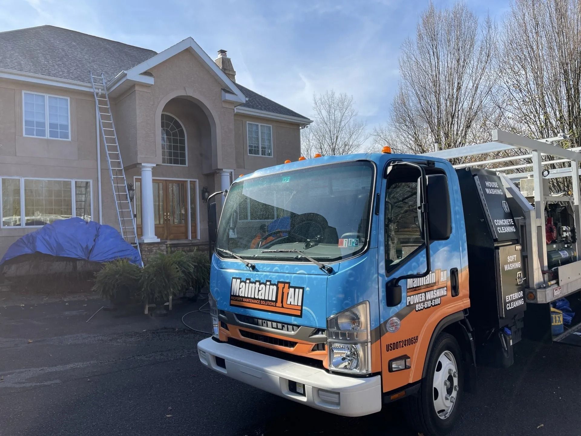 Blue truck with company logo parked in front of a house, ladder against the roof, covered item in front.