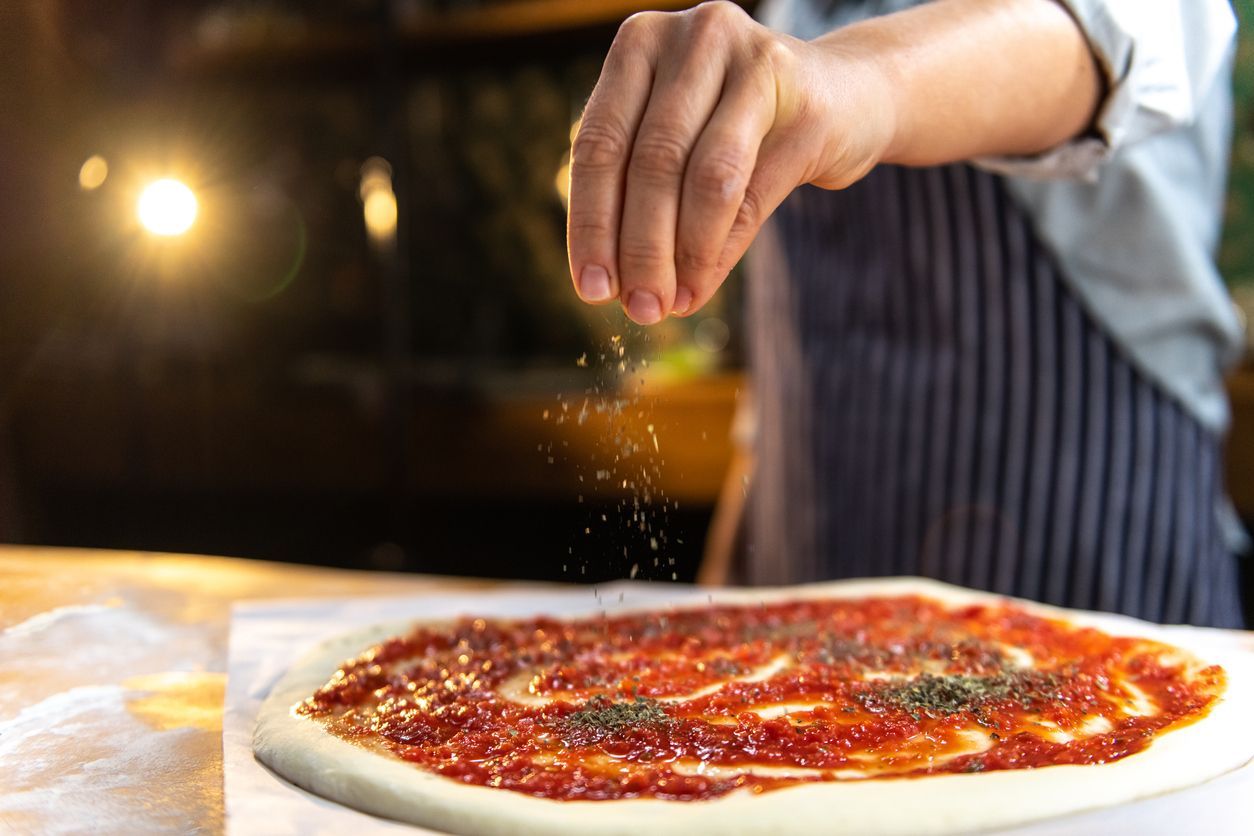 A person is sprinkling seasoning on a pizza.