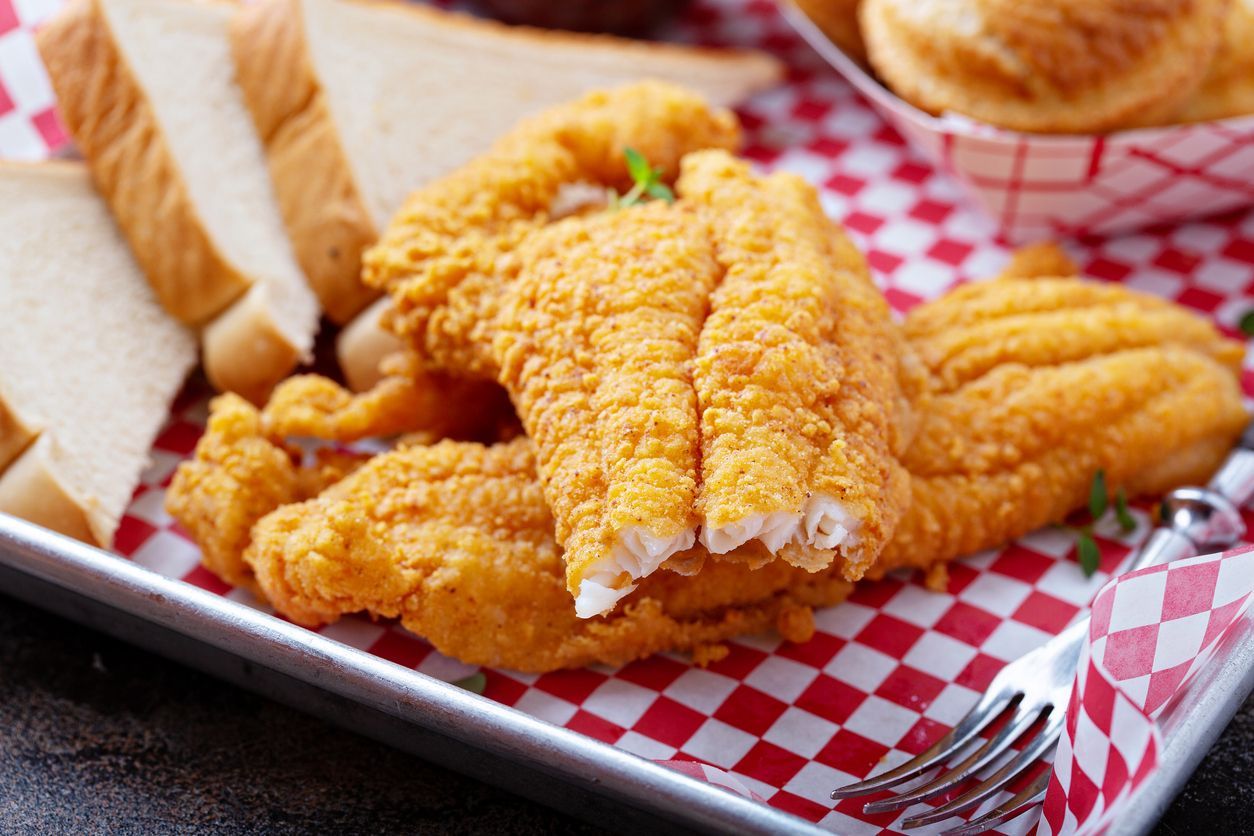 A tray of fried fish and bread on a checkered paper with a fork.