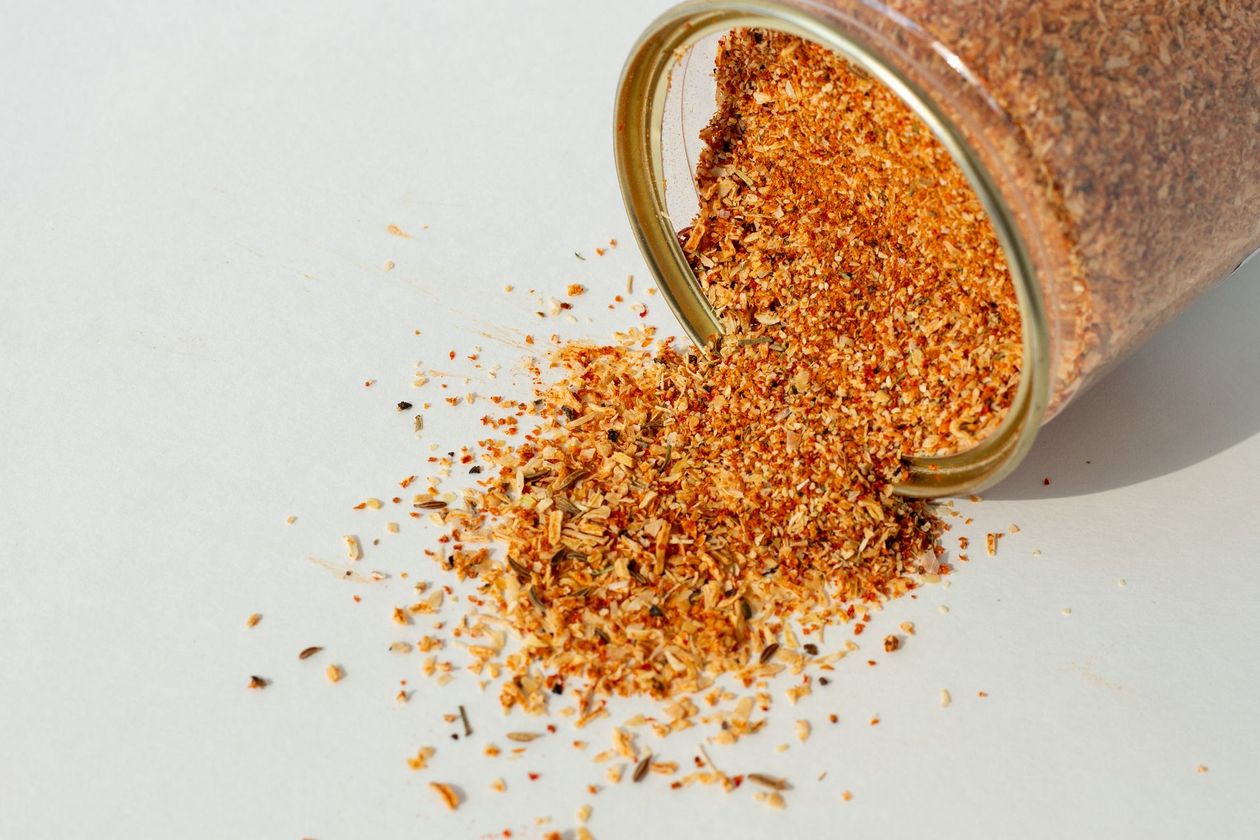 A jar of seasoning is spilling out onto a white surface.