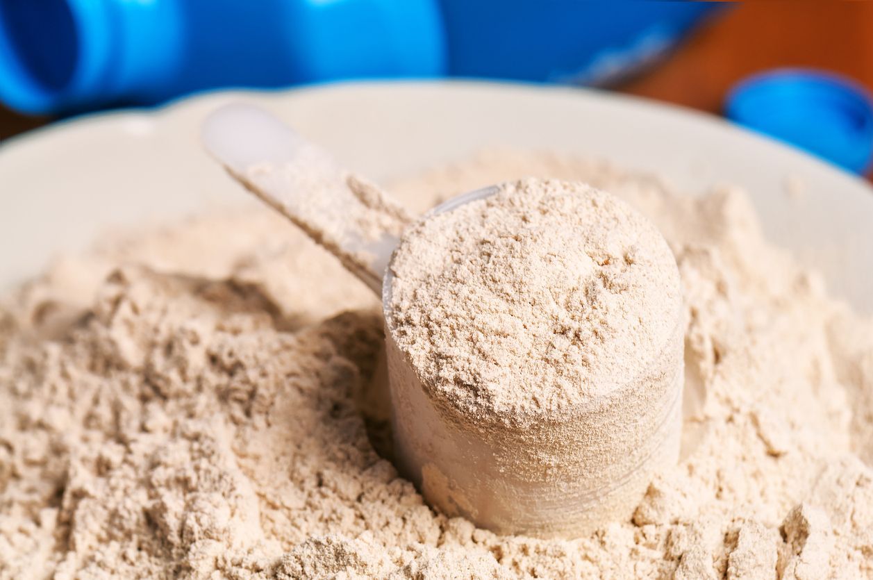 A measuring cup of protein powder is sitting on top of a pile of protein powder.