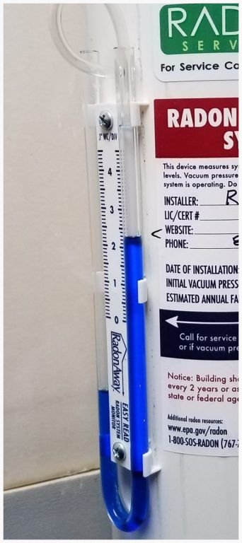 Blue Radon System Manometer attached to a radon mitigation pipe reading positive suction from fan.