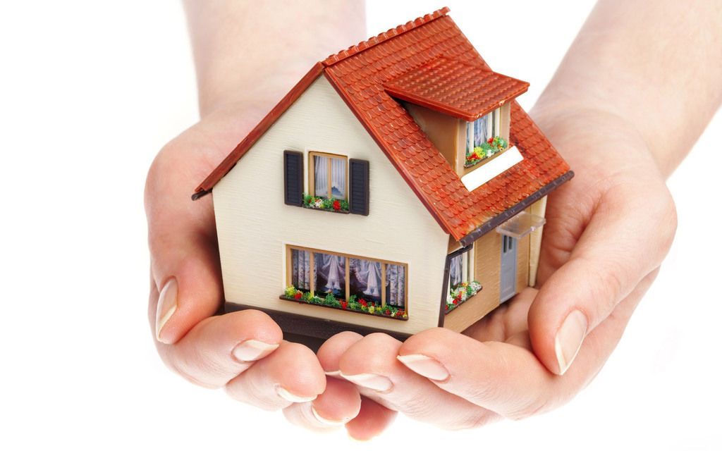 Hands cupping a miniature house with a red roof, symbolizing home ownership or security.