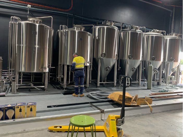 A Man Is Standing In Front Of A Row Of Stainless Steel Tanks In A Brewery — Hanby Welding & Engineering In Portsmith, QLD