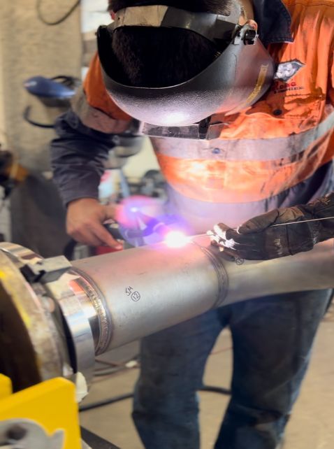 A Man Wearing A Welding Helmet Is Welding A Pipe — Hanby Welding & Engineering In Portsmith, QLD